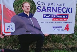 Kandydat Sarnecki w dziurze wyciętej we własnym bannerze