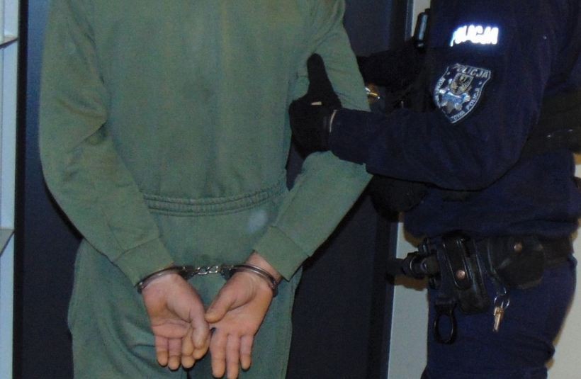 Policjant trzyma zatrzymanego w kajdankach